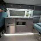 Interior view of Spartan Campers VW T6 SWB campervan showing the modern kitchen setup with built-in appliances, storage, and sleek two-tone cabinetry