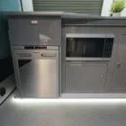 Interior view of Spartan Campers VW T6 SWB campervan showing the modern kitchen setup with built-in appliances, storage, and sleek two-tone cabinetry