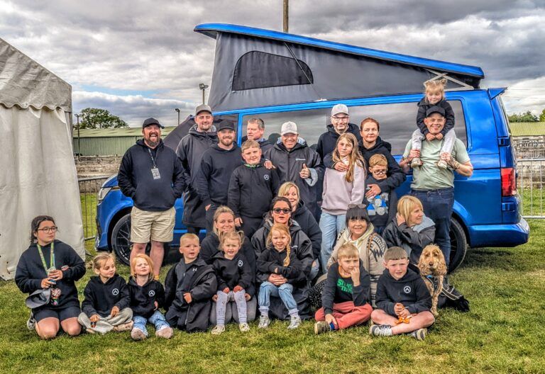 Spartan Campers family gathered around the VW campervan signed by Levi Roots during Campout 2025 at the Warners Show