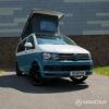 Iconic Spartan Campers marketing image of a VW T6 short wheelbase campervan, front-on with wheels turned inward, showcasing its bold stance and two-tone Neptune blue and candy white design