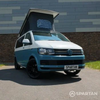 Iconic Spartan Campers marketing image of a VW T6 short wheelbase campervan, front-on with wheels turned inward, showcasing its bold stance and two-tone Neptune blue and candy white design