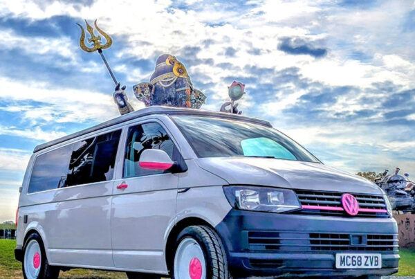 Custom Spartan VW campervan with pink accents parked at quirky roadside attraction, perfect for fun UK campervan adventures.