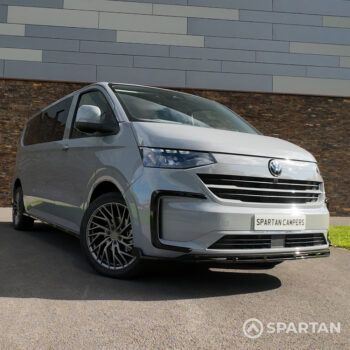 VW T7 driver-side front quarter angle showing modern aerodynamic lines, Volkswagen badge and Spartan camper styling details