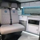 Stylish Spartan SWB campervan seating area with upholstered rock and roll bed beside kitchenette.