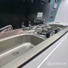 Spartan campervan galley kitchen setup with fridge, sink, and modern splashback beside passenger seats.