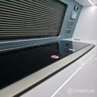 Spartan campervan galley kitchen setup with fridge, sink, and modern splashback beside passenger seats.