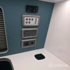 Spartan campervan galley kitchen setup with fridge, sink, and modern splashback beside passenger seats.