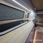 Modern campervan kitchen in latte and bardolino oak finish with built-in fridge, hob, and oak flooring.