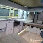 Modern campervan kitchen in latte and bardolino oak finish with built-in fridge, hob, and oak flooring.