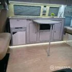 Luxury campervan interior showing latte cabinetry, natural bardolino oak accents, and rich liquor leather seating.