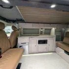Interior of Spartan Conversion VW T6 featuring winter flooring, latte main units with driftwood detailing, and liquor upholstery seating.