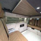 Interior of Spartan Conversion VW T6 featuring winter flooring, latte main units with driftwood detailing, and liquor upholstery seating.