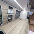 Interior of Spartan Conversion VW T6 featuring winter flooring, latte main units with driftwood detailing, and liquor upholstery seating.
