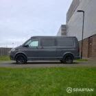 Volkswagen T6.1 long-wheelbase in Pure Grey, fitted with a Spartan camper conversion featuring the slide-and-swivel bench, clean interior lines and subtle exterior styling, parked outdoors.