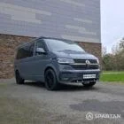 Volkswagen T6.1 long-wheelbase in Pure Grey, fitted with a Spartan camper conversion featuring the slide-and-swivel bench, clean interior lines and subtle exterior styling, parked outdoors.