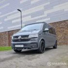 Volkswagen T6.1 long-wheelbase in Pure Grey, fitted with a Spartan camper conversion featuring the slide-and-swivel bench, clean interior lines and subtle exterior styling, parked outdoors.