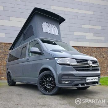 Volkswagen T6.1 long-wheelbase in Pure Grey, fitted with a Spartan camper conversion featuring the slide-and-swivel bench, clean interior lines and subtle exterior styling, parked outdoors.