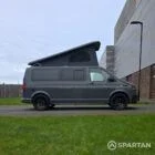Volkswagen T6.1 long-wheelbase in Pure Grey, fitted with a Spartan camper conversion featuring the slide-and-swivel bench, clean interior lines and subtle exterior styling, parked outdoors.