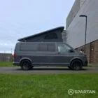 Volkswagen T6.1 long-wheelbase in Pure Grey, fitted with a Spartan camper conversion featuring the slide-and-swivel bench, clean interior lines and subtle exterior styling, parked outdoors.