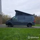 Volkswagen T6.1 long-wheelbase in Pure Grey, fitted with a Spartan camper conversion featuring the slide-and-swivel bench, clean interior lines and subtle exterior styling, parked outdoors.