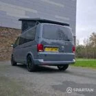 Volkswagen T6.1 long-wheelbase in Pure Grey, fitted with a Spartan camper conversion featuring the slide-and-swivel bench, clean interior lines and subtle exterior styling, parked outdoors.