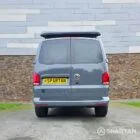 Volkswagen T6.1 long-wheelbase in Pure Grey, fitted with a Spartan camper conversion featuring the slide-and-swivel bench, clean interior lines and subtle exterior styling, parked outdoors.