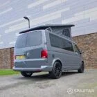 Volkswagen T6.1 long-wheelbase in Pure Grey, fitted with a Spartan camper conversion featuring the slide-and-swivel bench, clean interior lines and subtle exterior styling, parked outdoors.