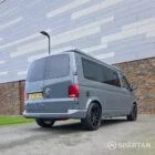 Volkswagen T6.1 long-wheelbase in Pure Grey, fitted with a Spartan camper conversion featuring the slide-and-swivel bench, clean interior lines and subtle exterior styling, parked outdoors.