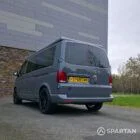 Volkswagen T6.1 long-wheelbase in Pure Grey, fitted with a Spartan camper conversion featuring the slide-and-swivel bench, clean interior lines and subtle exterior styling, parked outdoors.