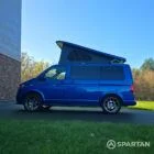 VW T6.1 Transporter in Ravenna Blue, fitted with a Spartan campervan conversion, parked outdoors. Clean lines, factory stance, and upgraded camper profile visible