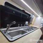VW T7 Transporter with Spartan campervan conversion interior with latte and amber oak kitchen with twin gas burner and sink lid open and savvy van digital display