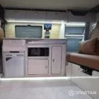 VW T7 Transporter with Spartan campervan conversion interior with winter flooring, latte and amber oak kitchen and fudge upholstery. Kitchen with fridge freezer, microwave, fabworks r&r bed and savvy van digital display