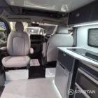 VW T7 Transporter with Spartan campervan conversion. Interior view with blizzard flooring, storm cloud and light grey kitchen showcasing the front captains swivel seat in the living area
