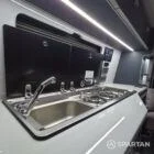 VW T7 Transporter with Spartan campervan conversion. Interior view with blizzard flooring, storm cloud and light grey kitchen showcasing the sink and twin gas burner with the lid open