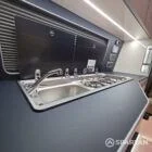 VW T6.1 interior of a Spartan campervan conversion, fitted with altro flooring, ivory and indigo blue kitchen and taupe upholstery. Featuring a microwave, fridge/ freezer, wireless fast charger, sink, double gas burner and central control panels
