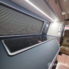 VW T6.1 interior of a Spartan campervan conversion, fitted with altro flooring, ivory and indigo blue kitchen and taupe upholstery. Featuring a microwave, fridge/ freezer, wireless fast charger, sink, double gas burner and central control panels