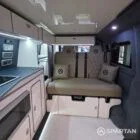 VW T6.1 interior of a Spartan campervan conversion, fitted with altro flooring, ivory and indigo blue kitchen and taupe upholstery. Featuring a microwave, fridge/ freezer, wireless fast charger, sink, double gas burner and central control panels