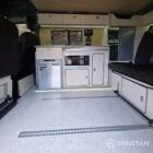VW T7 Short wheelbase Spartan campervan interior with a passenger bench seat and mobiframe bed on rails. Winter flooring, latte and winchester oak kitchen