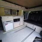 VW T7 Short wheelbase Spartan campervan interior with a passenger bench seat and mobiframe bed on rails. Winter flooring, latte and winchester oak kitchen