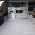 SWB VW T7 with Spartan Campers conversion, interior with winter flooring, latte and Italian reed green kitchen, liquor upholstery. Including a microwave, fridge/ freezer, rock and roll bed, double gas burner and sink