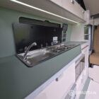 SWB VW T7 with Spartan Campers conversion, interior with winter flooring, latte and Italian reed green kitchen, liquor upholstery. Including a microwave, fridge/ freezer, rock and roll bed, double gas burner and sink