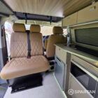 View towards the front cabin showing the passenger double bench seat, central aisle and modern camper interior.